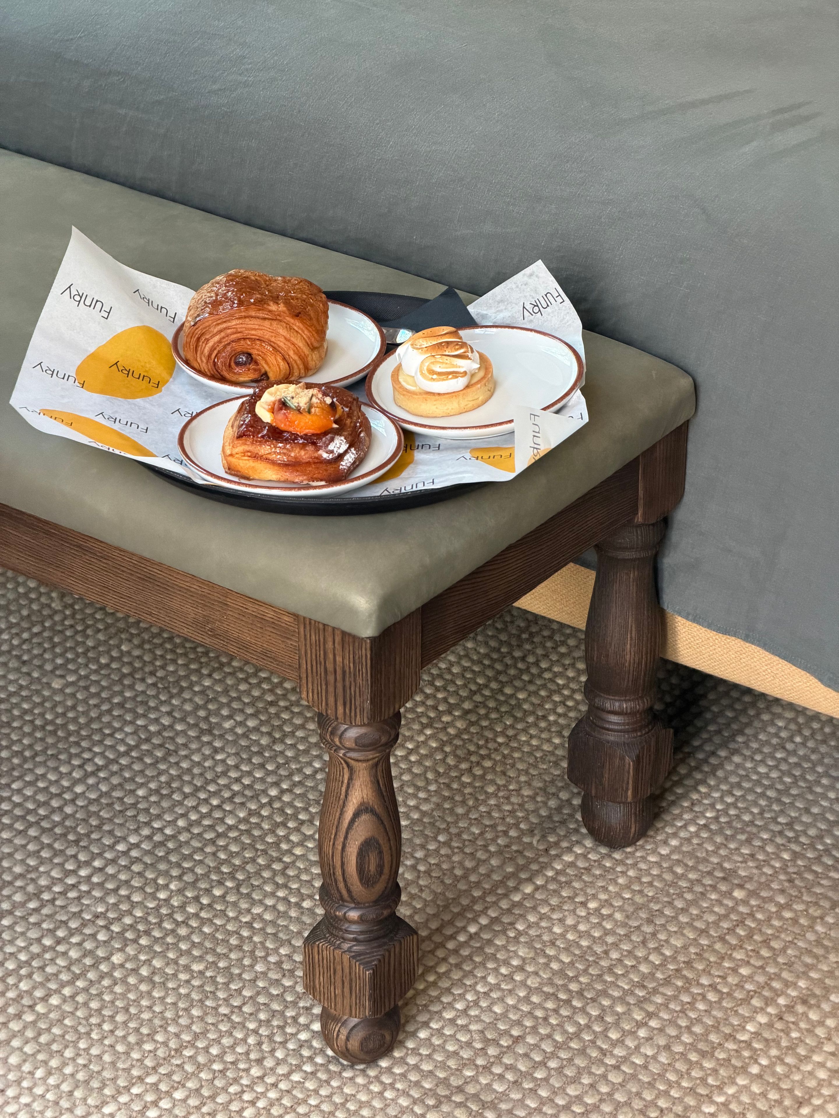 Breakfast with a croissant, pastry, and coffee served on a tray placed on a stool in a Borneta hotel room.