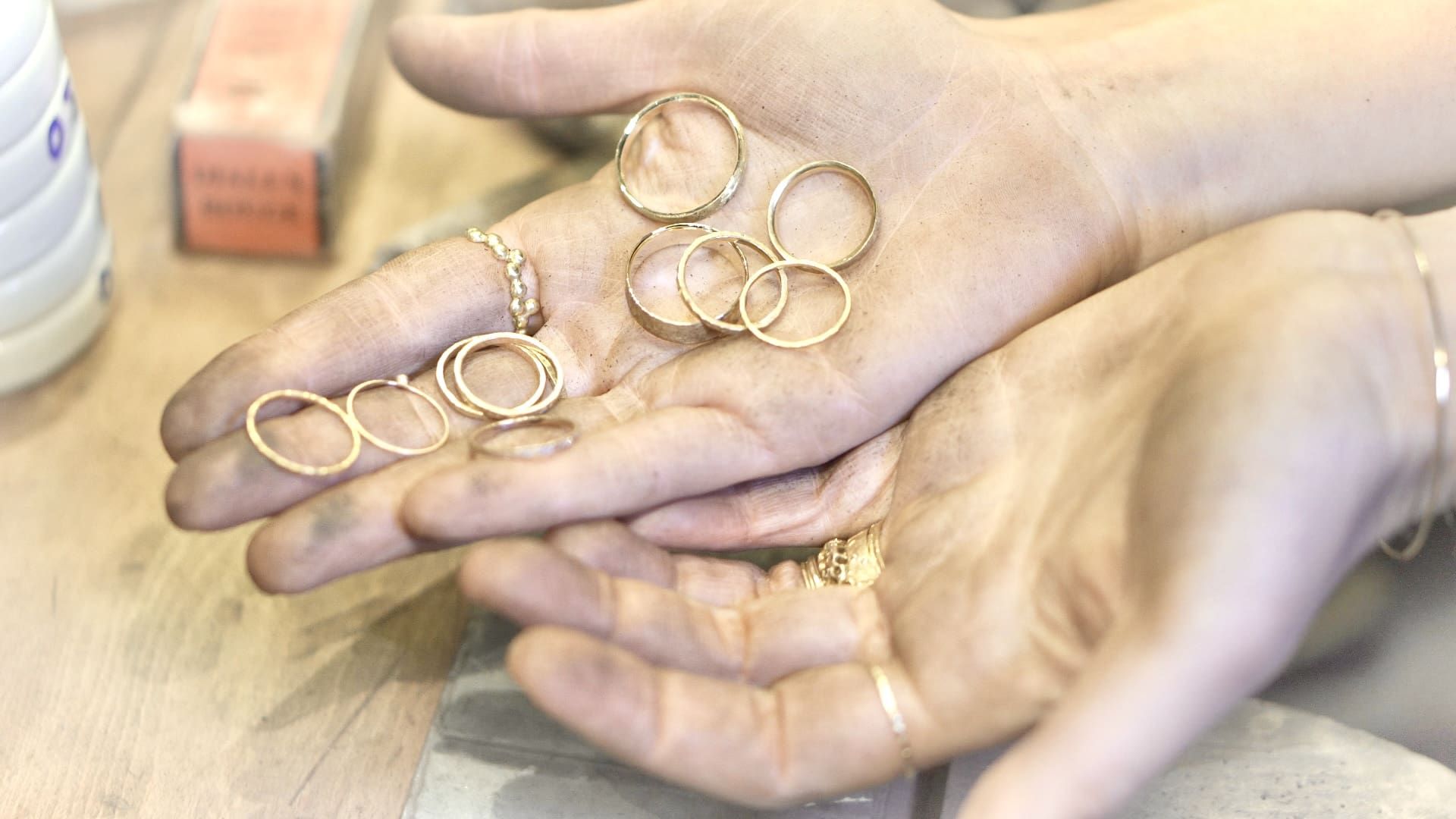 Hand holding several handmade gold rings in the jewelry workshop.